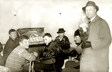 Ordf&oslash;rer Arne S&aelig;ter bes&oslash;ker kafeen p&aring; Rindal sentrum. Rundt jukeboksen sitter fra venstre Odd Jostein S&aelig;ter, Johan Landsem, Leif Arne Lj&oslash;kjell, Lars Bakken og Peder Rindalsholt. Rindal, 1965.
