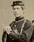 John L. Sæther i militæruniform med sin 12 mm Remington rolling block-rifle produsert på Kongsberg Våpenfabrikk. Full militær utrustning, i menig infanteriuniform.
